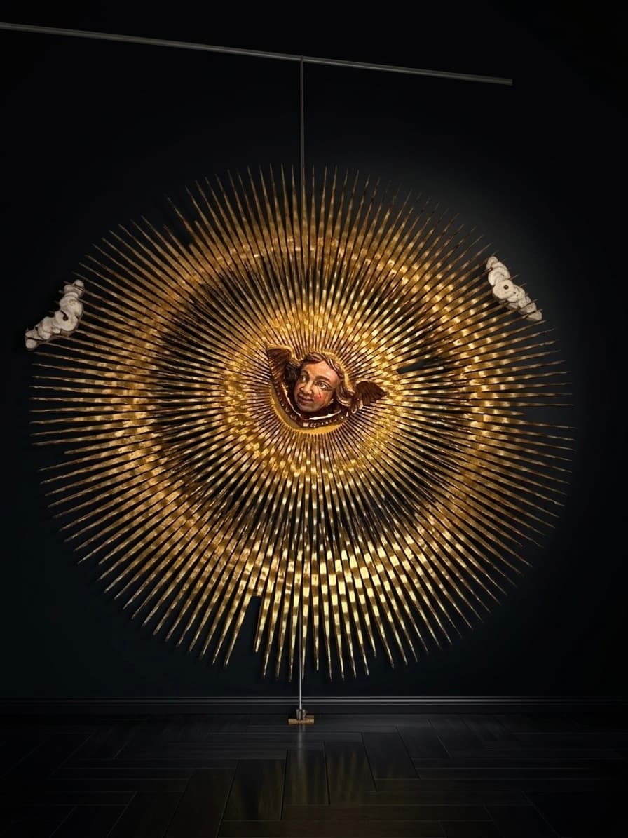 Gran sol dorado tallado con un rostro de ángel central sobre un fondo oscuro.