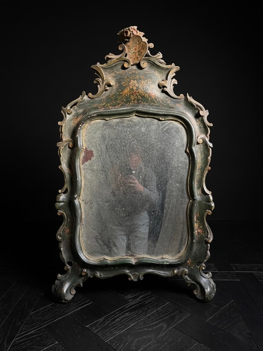 Espejo antiguo con marco verde ornamentado, detalles florales y cristal envejecido sobre fondo negro.