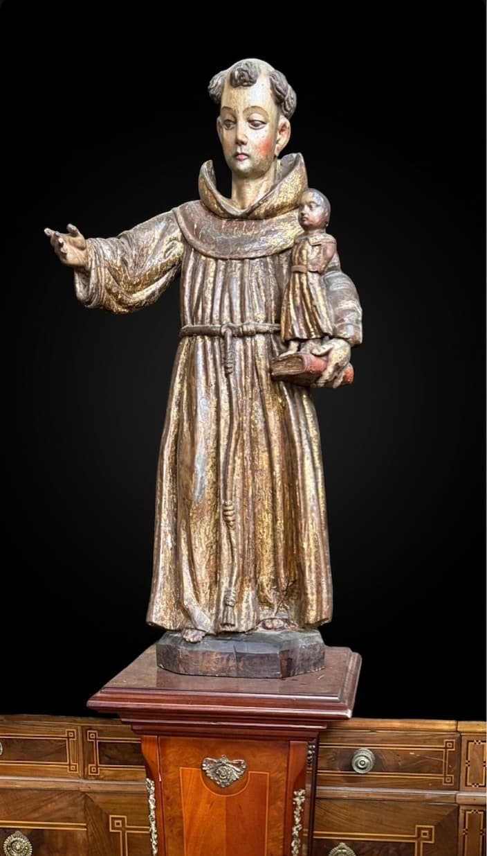 Escultura de madera de San Antonio de Padua sosteniendo al Niño Jesús sobre un libro.