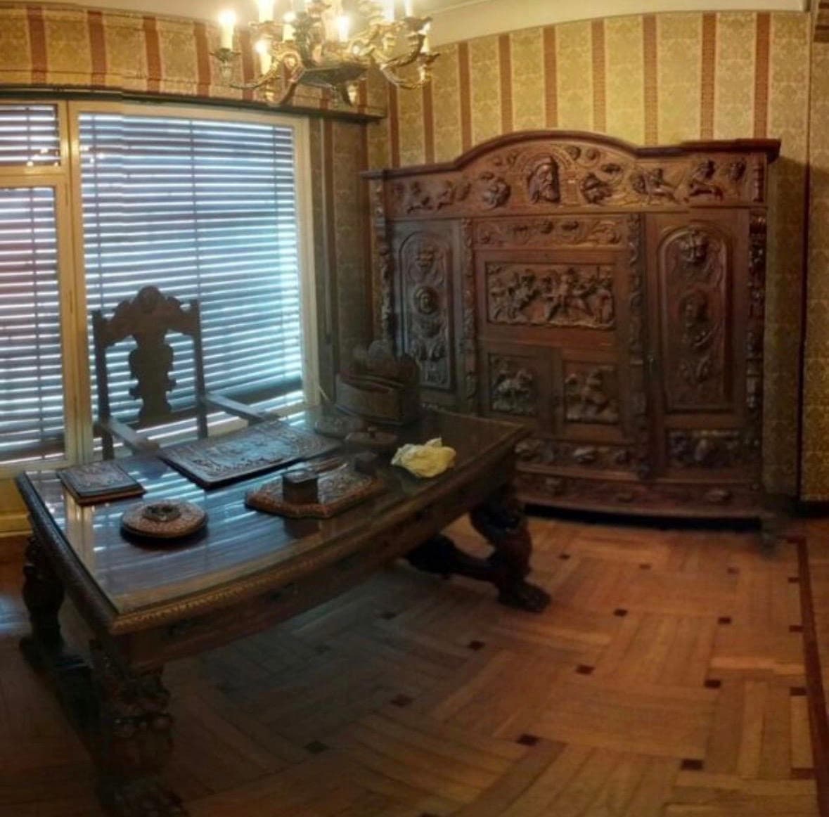 Escritorio de madera tallada y armario antiguo ornamentado en una habitación con suelo de parqué.